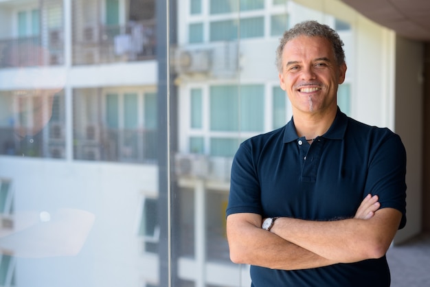 Portret van volwassen knappe man door het glazen raam van moderne, eigentijdse woning binnenshuis