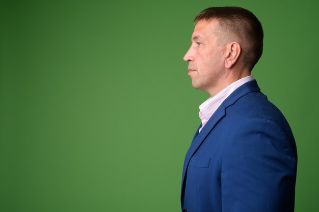 Portret van volwassen machozakenman die blauw kostuum tegen Chromakey met groene muur dragen