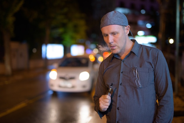 Portret van volwassen man elektronische sigaret roken in de straten 's nachts