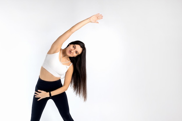 Foto portret van volwassen meisje haar armen uitrekken op witte achtergrond aantrekkelijke brunette vrouw in modieuze sportkleding uitoefening gezonde levensstijl sport concept