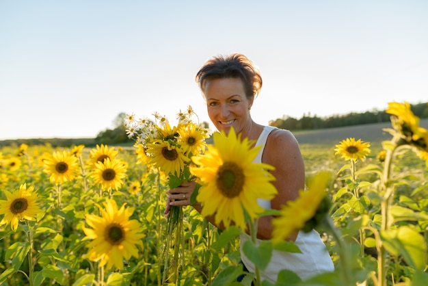 Portret van volwassen mooie Scandinavische vrouw op het gebied van bloeiende zonnebloemen buitenshuis