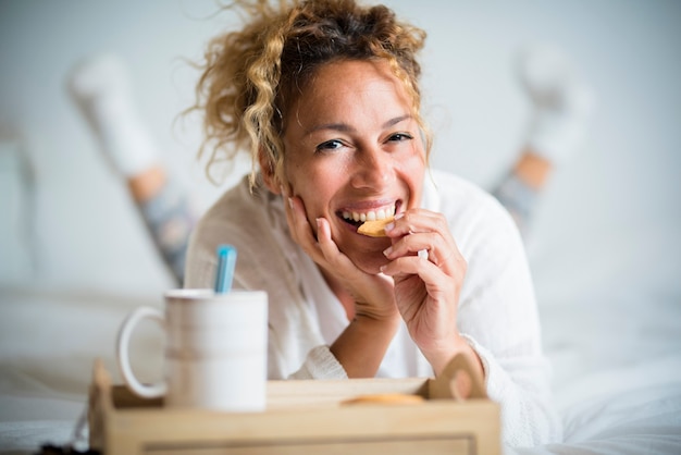 Portret van volwassen mooie vrouw die koekje eet in het ochtendontbijt in de slaapkamer