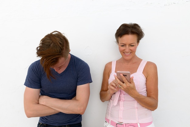 Portret van volwassen vrouw en jonge man als moeder en zoon samen tegen witte muur als muur buitenshuis