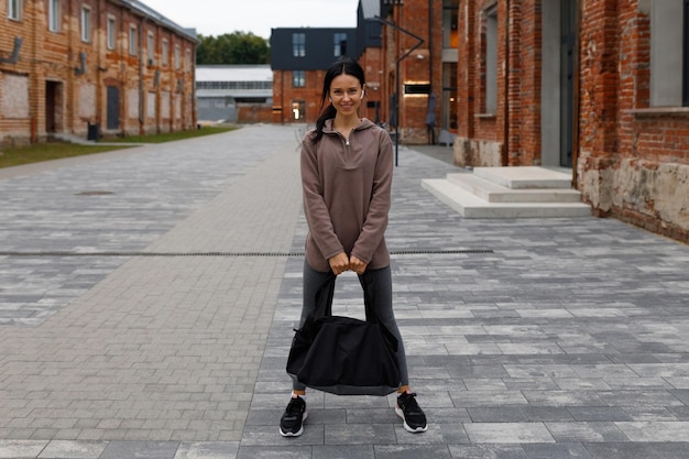 Portret van volwassen vrouw met sporttas in de buurt van sportschool