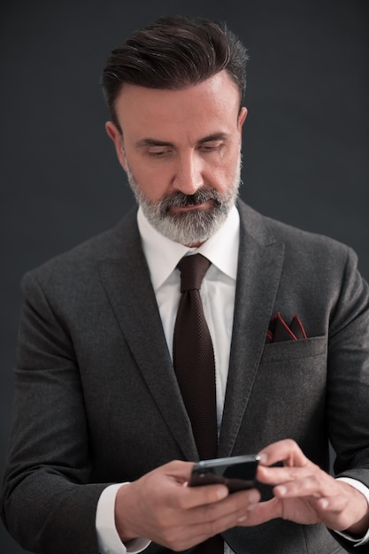 Portret van volwassen zakenman die trendy pak draagt en in moderne studio op stijlvolle stoel tegen de zwarte achtergrond zit. Horizontaal model. Hoge kwaliteit foto