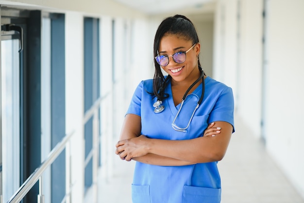 Portret van vriendelijke, glimlachende zelfverzekerde vrouwelijke zorgverlener met laboratoriumjas, gekruiste armen met een bril. Geïsoleerde ziekenhuis kliniek achtergrond.