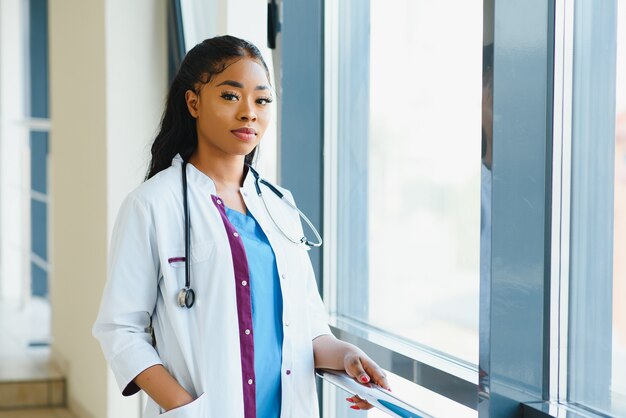 Portret van vriendelijke, glimlachende zelfverzekerde vrouwelijke zorgverlener met laboratoriumjas, gekruiste armen met een bril. Geïsoleerde ziekenhuis kliniek achtergrond.