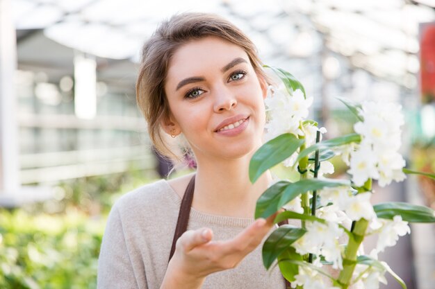 Portret van vrij gelukkige jonge vrouwentuinman met witte bloeiende orchidee in oranjerie