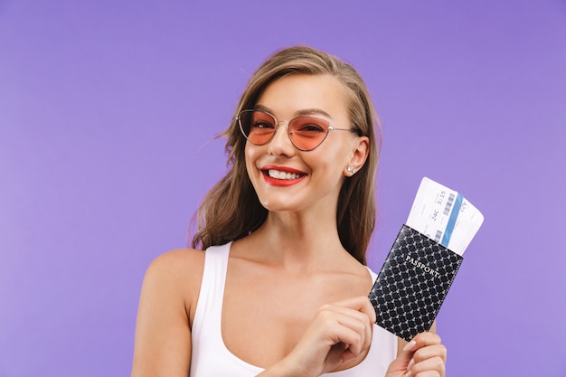 Portret van vrij gelukkige vrouw in de zomerkleren en zonnebril die en paspoort en reiskaartjes glimlachen houden,