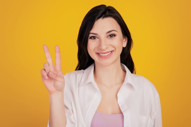 Portret van vrij schattig positief meisje toont v-teken op gele achtergrond