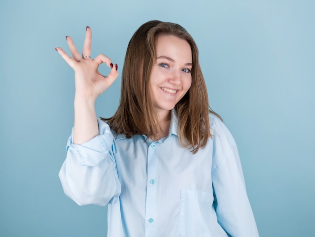 Portret van vrolijk jong wijfje dat normaal gebaar in denimoverhemd toont dat op blauw wordt geïsoleerd