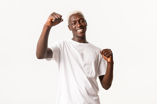 Portret van vrolijke afro-amerikaanse blonde kerel, gelukkig winnen en glimlachen, zich verheugen over winnen en triomferen.