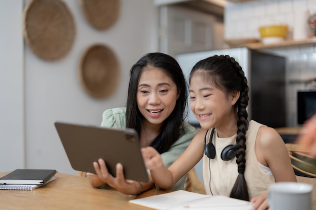 Portret van vrolijke Aziatische moeder en dochter die thuis digitale tablet in keuken gebruiken