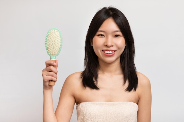 Portret van vrolijke Aziatische vrouw die haar haar borstelt