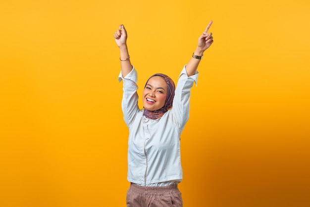 Portret van vrolijke Aziatische vrouw met overwinningsuitdrukking over gele background