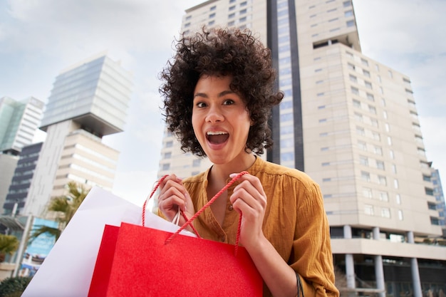 Foto portret van vrolijke jonge afrikaans-amerikaanse vrouwelijke shopaholic met verbaasde papieren zakken aan het winkelen