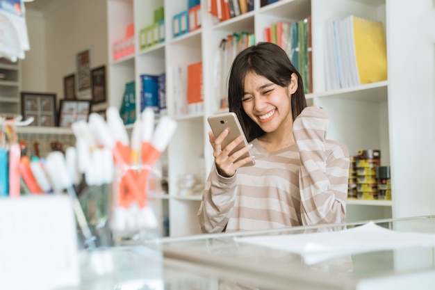 Portret van vrolijke jonge ondernemer blij om bestellingen via mobiel te zien werken in een kantoorboekhandel