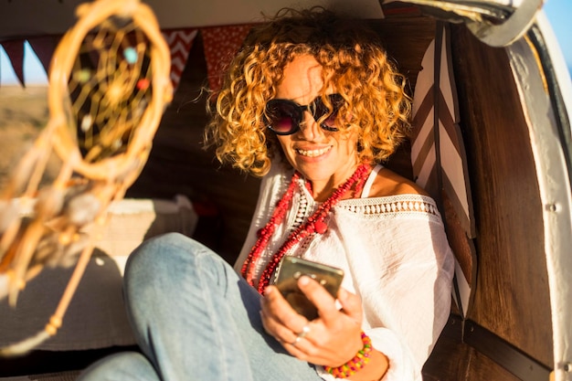 Portret van vrolijke jonge volwassen vrouw met behulp van telefoon zitten en genieten in klassieke reisbus voertuig Mooie vrouwelijke mensen met verbinding cellulaire technologie en planning road trip voor vakantie