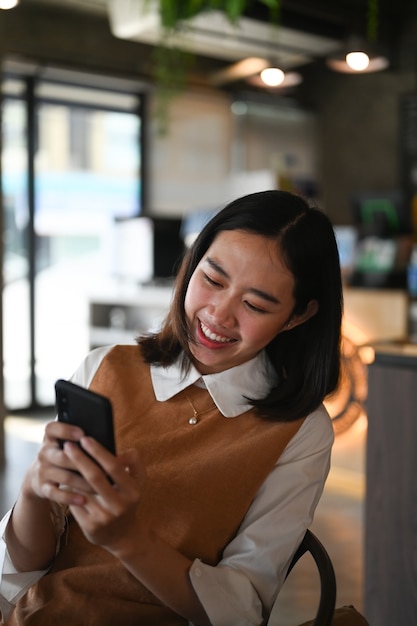 Portret van vrolijke jonge vrouw surfen op draadloos internet op smartphone zittend in café.