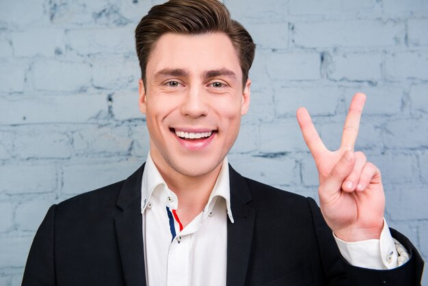 Foto portret van vrolijke jonge zakenman gebaren met twee vingers