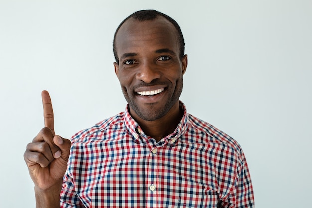 Portret van vrolijke knappe afro Amerikaanse man die lacht terwijl het uitleggen van regels tegen witte muur