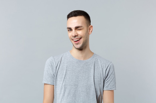 Portret van vrolijke knipperende grappige jonge man in casual kleding permanent