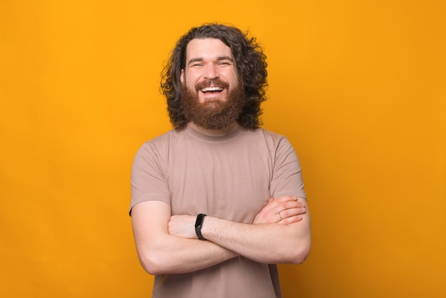 Portret van vrolijke lachende bebaarde hipster man met gekruiste armen over geel kijken naar de camera