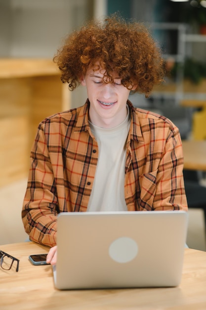 Portret van vrolijke millennial blogger met moderne mobiele telefoon en laptop technologie genieten van freelance levensstijl gelukkig hipster man in optische brillen met behulp van mobiele telefoon en netbook in straatcafé