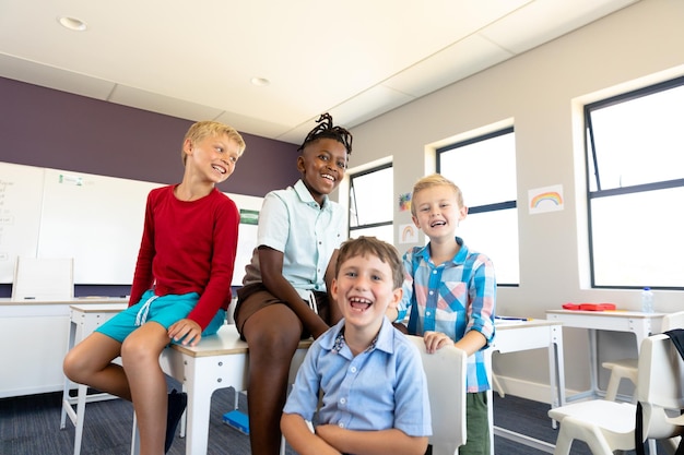 Foto portret van vrolijke multiraciale basisschooljongens die aan het bureau in de klas zitten