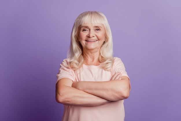 Portret van vrolijke oude volwassen vrouw staan met gekruiste armen over violette achtergrond