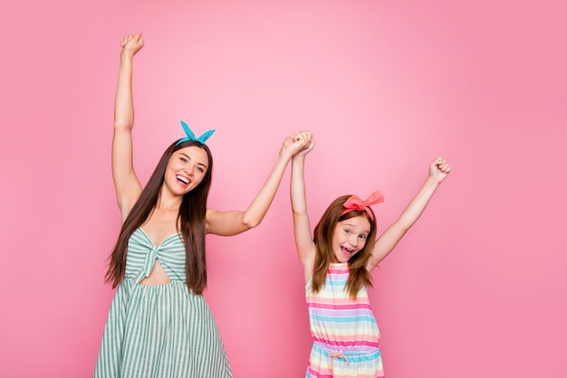 Portret van vrolijke twee vrouwen die handen houden die de rok van de hoofdbandenkleding dragen die over roze achtergrond wordt geïsoleerd