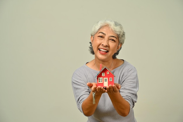 Portret van vrolijke volwassen vrouw met huismodel geïsoleerd op beige achtergrond Onroerend goed gebouw eigendom en verzekeringen