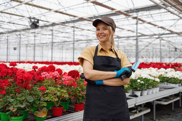 Portret van vrolijke vrouwelijke bloemist met handtroffel in bloemenkas