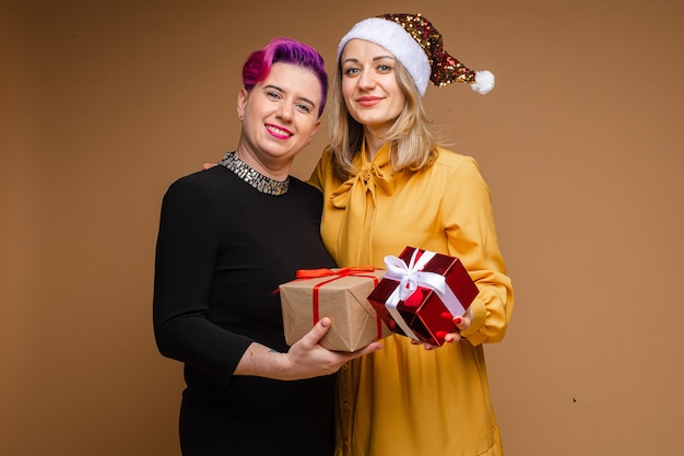 Portret van vrolijke vrouwen uitwisselen van kerstcadeaus en glimlachen. Blonde draagt sprankelende kerstmuts en gele jurk