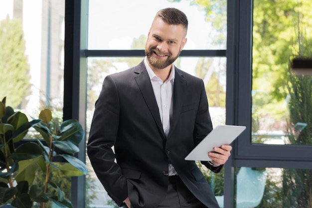 Portret van vrolijke zakenman met digitale tablet in handen camera kijken