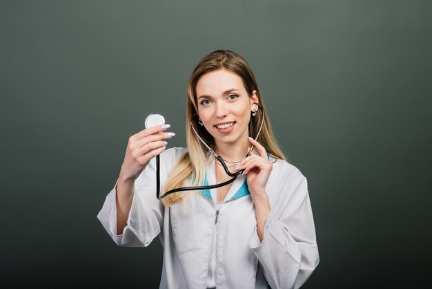 Portret van vrouw arts met een stethoscoop camera kijken op grijze achtergrond