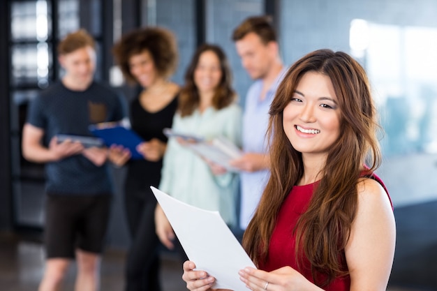 Portret van vrouw die een document leest terwijl collega&#39;s die zich erachter in bureau bevinden