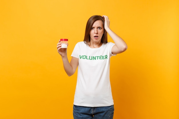 Portret van vrouw in wit t-shirt geschreven inscriptie groene titel vrijwilliger met fles met pillen drug geïsoleerd op gele achtergrond. Vrijwillige gratis hulp, liefdadigheidsgezondheidsconcept.