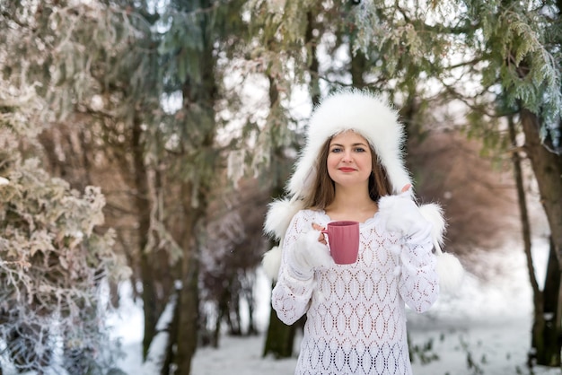 Portret van vrouw in witte trui en hoed buiten op koude winterdag sneeuwt.