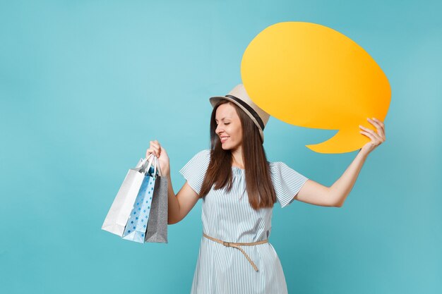 Portret van vrouw in zomerjurk, strohoed met pakketten met tassen met aankopen na het winkelen, lege blanco Say cloud, tekstballonkaart geïsoleerd op blauwe pastelachtergrond. Ruimte advertentie kopiëren