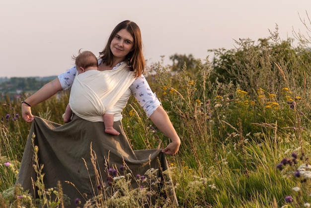 Foto portret van vrouw met baby die in stof draagt terwijl ze rok vasthoudt op het veld tegen de lucht