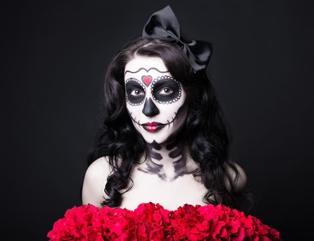 portret van vrouw met creatieve Halloween schedel make-up en rode bloemen op zwarte achtergrond