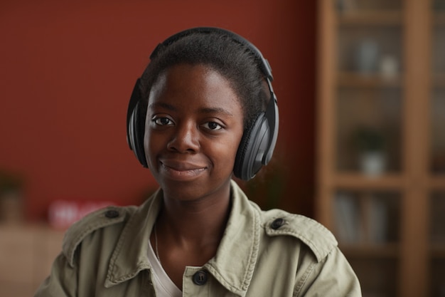 Portret van vrouwelijke Afro-Amerikaanse muzikant hoofdtelefoon dragen en camera kijken tijdens het componeren thuis, kopieer ruimte