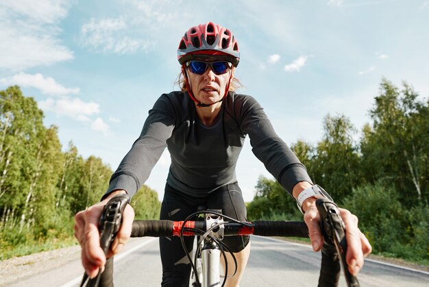 Portret van vrouwelijke atleet in helmzonnebril en sportkleding die op een fiets rijdt