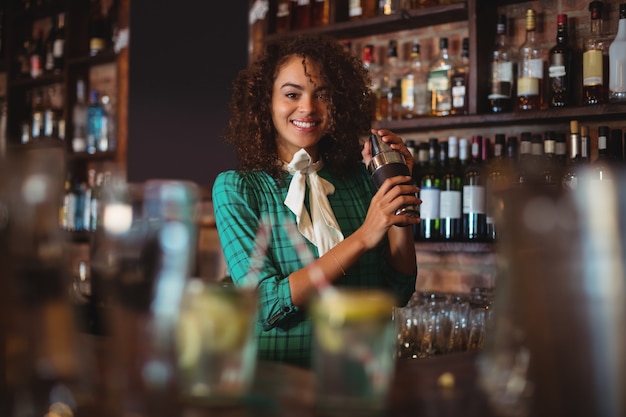 Portret van vrouwelijke barman die een cocktaildrankje in cocktailshaker mengt