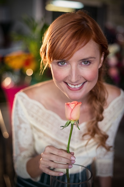 Portret van vrouwelijke bloemist die een roze bloem ruikt