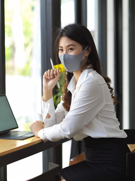 Portret van vrouwelijke dragen masker werken met digitale tablet in café