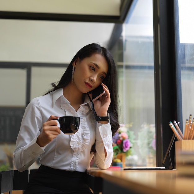 Portret van vrouwelijke freelancer praten aan de telefoon tijdens een koffiepauze op de werkplek