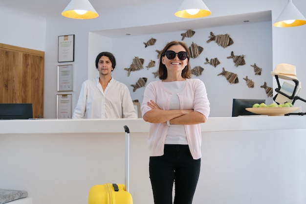 Portret van vrouwelijke gast met koffer, mannelijke hotelarbeider dichtbij receptie