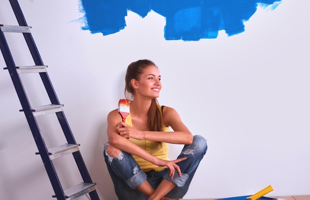 Portret van vrouwelijke schilderszitting op vloer dichtbij muur na het schilderen